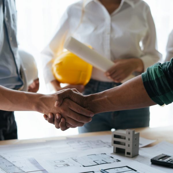 Construction workers, architects and engineers shake hands after completing an agreement in an office facility, successful cooperation concept.